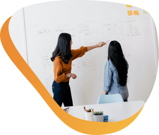 Woman explaining to another female marketing professional how to increase direct-response marketing activity on a whiteboard